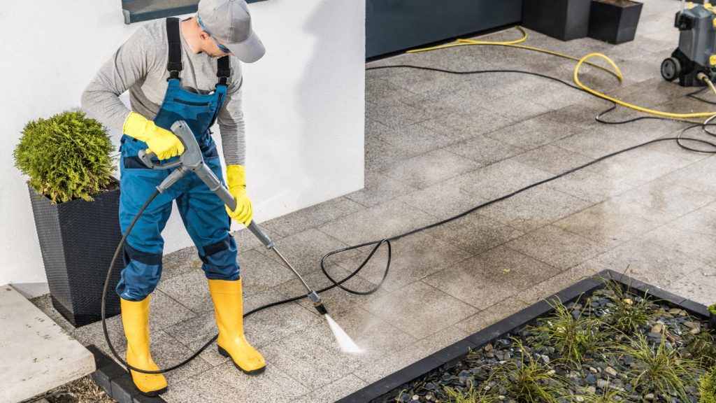 Worker using pressure washer on concrete driveway in Prime Hook, DE residential area
