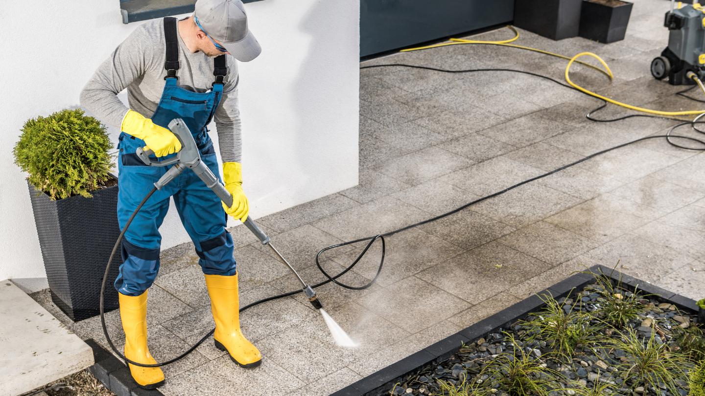 Worker using pressure washer on concrete driveway in Prime Hook, DE residential area